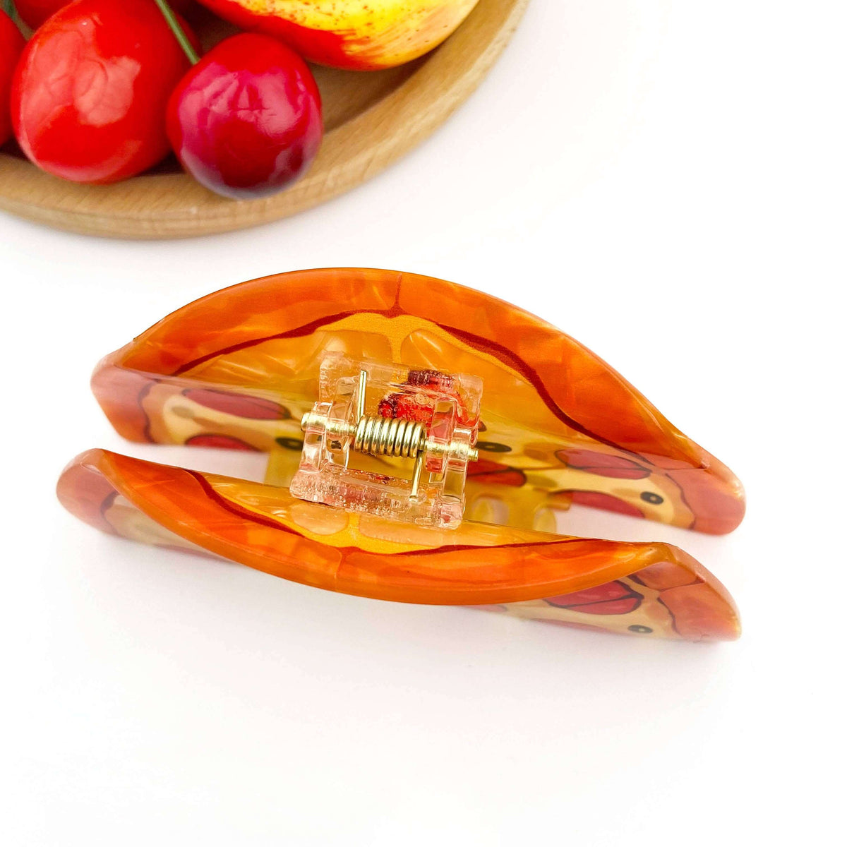 Pizza hair claw clip in orange design, resembling a ham pizza slice, surrounded by colorful fruits.