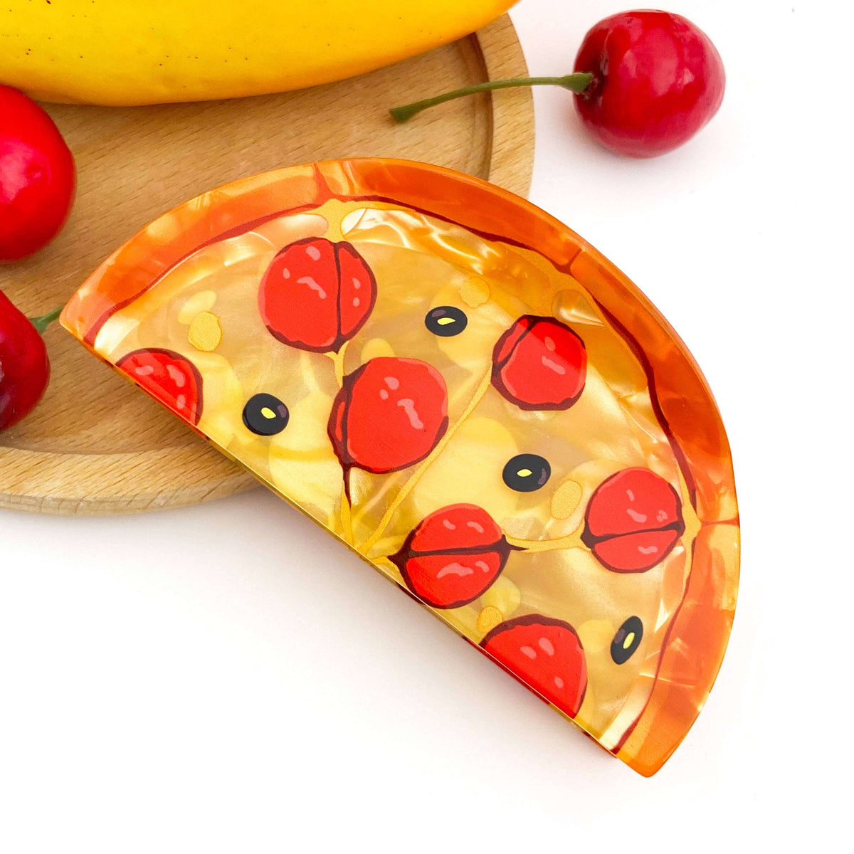 Pizza hair claw clip designed as a colorful ham pizza slice on a wooden plate with fruit.