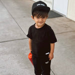 Toddler wearing a black wild child toddler snapback hat and matching outfit while holding a toy.