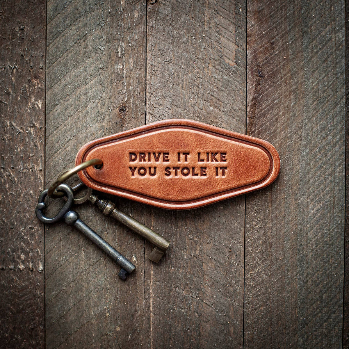 Leather keychain motel style featuring 'Drive It Like You Stole It' text on a wooden background.