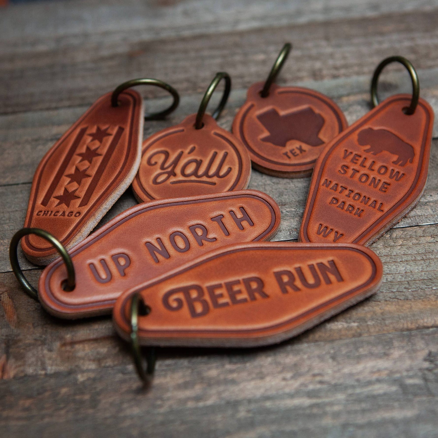 Leather keychain motel style collection with phrases like Up North and Beer Run on wooden background.